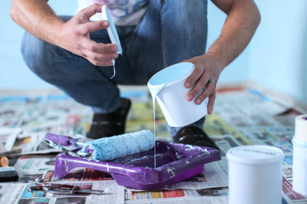 Homme accroupi en train de verser un pot de peinture blanche dans un bac